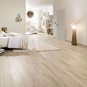 Ein weißes Bett in einem hellen Schlafzimmer mit Linoelumboden