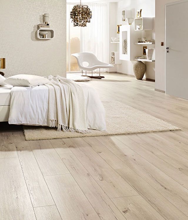 Ein weißes Bett in einem hellen Schlafzimmer mit Laminatboden